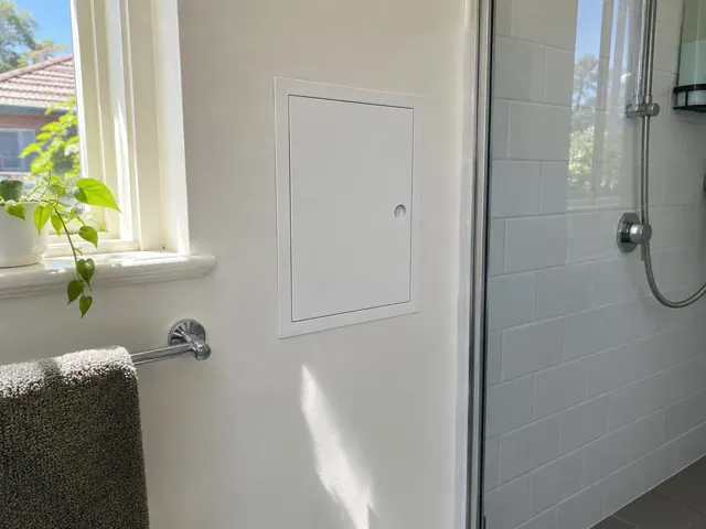Neat white access panel on a bathroom wall beside a tiled shower and window in Normanhurst