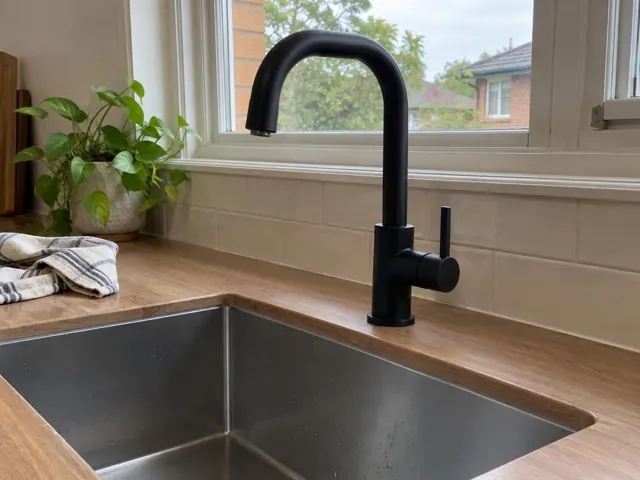 Matte black kitchen mixer above a stainless steel sink, with tiled splashback and window in Beecroft